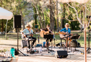 Outdoor live band performing among trees in the sunlight at Huttopia Parque de Doñana, Andalusia, Spain.
