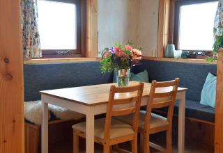 Acogedor rincón de comedor con mesa de madera, flores frescas y bancos en una casa del árbol en los Países Bajos.