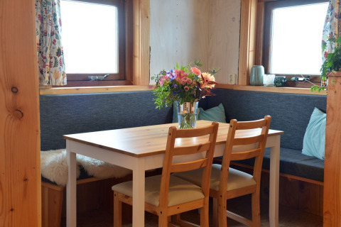 Acogedor rincón de comedor con mesa de madera, flores frescas y bancos en una casa del árbol en los Países Bajos.