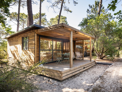 Cabaña de madera con terraza cubierta en un entorno forestal en Huttopia Parque de Doñana, Andalucía, España.
