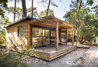 Cabaña de madera con terraza cubierta en un entorno forestal en Huttopia Parque de Doñana, Andalucía, España.