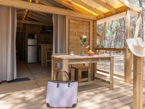 Terraza de madera con mesa, bolso y flores en Huttopia Parque de Doñana, parque vacacional en Andalucía, España.