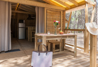 Houten terras met tafel, tas en bloemen bij Huttopia Parque de Doñana, vakantiepark in Andalusië, Spanje.