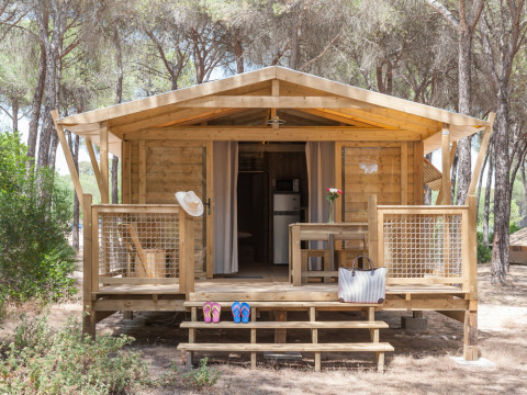 Cabaña de madera en Huttopia Parque de Doñana, Andalucía, España, rodeada de árboles, con porche y decoración.