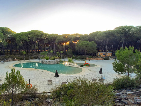 Vista de piscina con arena rodeada de bosque al atardecer en Huttopia Parque de Doñana, Andalucía, España.