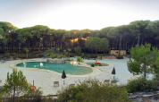 Udsigt over en swimmingpool omgivet af sand og skov ved solnedgang i Huttopia Parque de Doñana, Andalusien.