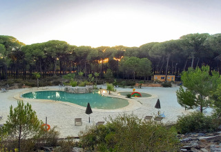 Blick auf einen Pool mit Sandstrand und Liegestühlen im Huttopia Parque de Doñana, Andalusien, bei Sonnenuntergang.