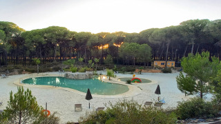 Zicht op een zwembad met zandstrand tussen het bos bij zonsondergang in Huttopia Parque de Doñana, Andalusië.