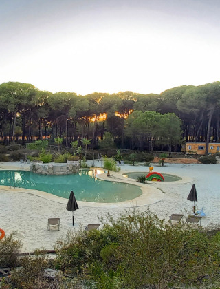 Vista de piscina con arena rodeada de bosque al atardecer en Huttopia Parque de Doñana, Andalucía, España.
