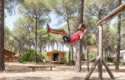 Barn gynger på legeplads i skov ved træhytter i Huttopia Parque de Doñana, feriepark i Andalusien, Spanien.