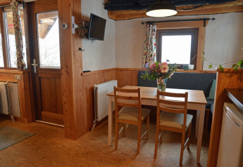 Gezellige eettafel in een boomhut met houten muren, bloemen en ramen op een campinglocatie.