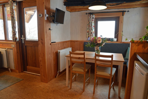 Gezellige eettafel in een boomhut met houten muren, bloemen en ramen op een campinglocatie.