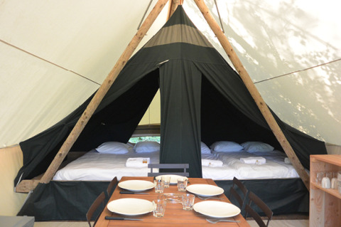 Interior de una tienda safari Canadienne con camas y mesa de comedor en Huttopia Parque de Doñana, España.
