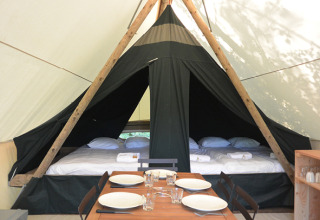 Interior de una tienda safari Canadienne con camas y mesa de comedor en Huttopia Parque de Doñana, España.