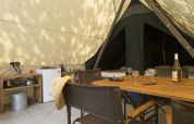 Interior de una tienda safari Canadienne con mesa de madera, utensilios de cocina y camas al fondo.