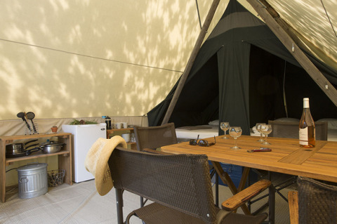 Innenansicht eines Safari-Zeltes Canadienne mit Holztisch, Stühlen, Kühlschrank und Kochutensilien.