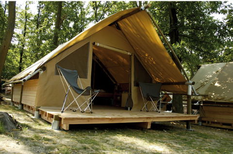 Canadienne Safari-Zelt mit Holzterrasse und zwei Campingstühlen in einem bewaldeten Gebiet.