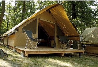 Tente safari Canadienne avec terrasse en bois et deux fauteuils, située dans une forêt verdoyante.