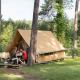 En familie sidder udenfor en Canadienne safari telt omgivet af grønne træer på en campingplads.