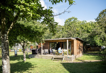 Chalet Portland in het zonlicht met gasten op het terras, omgeven door groene bomen en natuur.