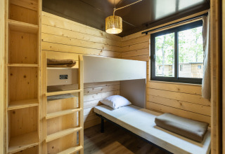 Cama individual y estanterías de madera en Chalet Portland de Huttopia Parque de Doñana, España.