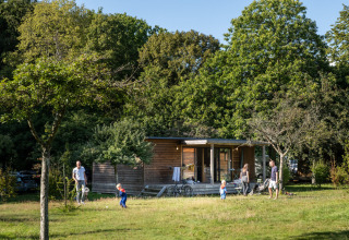 Familie nyder udendørs tid foran Chalet Portland ved Huttopia Parque de Doñana, omgivet af grønne træer.
