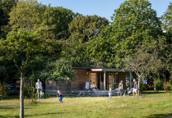 Familie entspannt sich vor Chalet Portland im Huttopia Parque de Doñana, umgeben von viel Grün.
