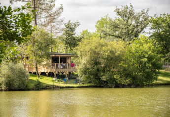 Houten chalet Chalet Portland aan een meer in Huttopia Parque de Doñana, Spanje, omgeven door bomen.
