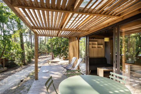 Terraza exterior con pérgola de madera y zona de estar en Chalet Portland, Huttopia Parque de Doñana, España.
