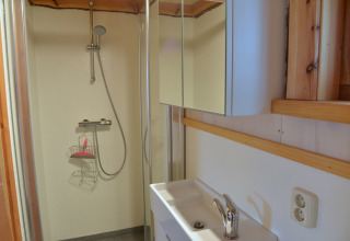 Baño con ducha y armario con espejo en la casa del árbol Ooievaarsnest en Camping de Koeksebelt, Países Bajos.