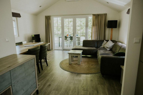 Wohnbereich in der Forest Lodge auf Camping Si-Es-An in den Niederlanden mit Sofa und Gartentür.