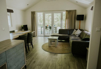 Sala moderna en Forest Lodge, Camping Si-Es-An, Países Bajos, con sofá, mesa y puertas hacia la terraza.