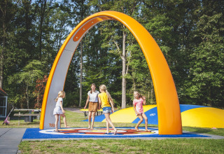 Niños jugando bajo un gran arco naranja en Camping de Koeksebelt en los Países Bajos, rodeados de árboles.