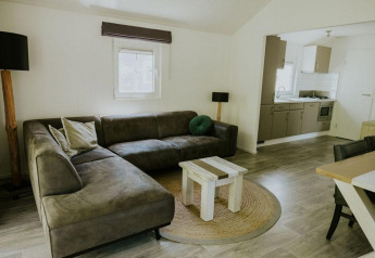 Sala de estar en Forest Lodge, Camping Si-Es-An, Países Bajos, con sofá esquinero, mesa y cocina.