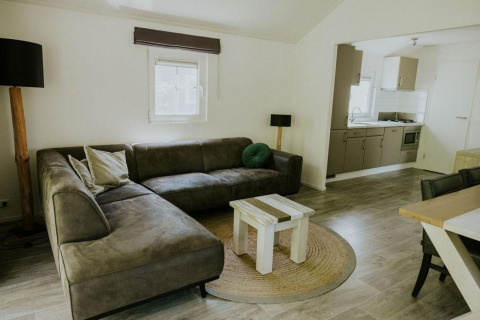 Sala de estar en Forest Lodge, Camping Si-Es-An, Países Bajos, con sofá esquinero, mesa y cocina.