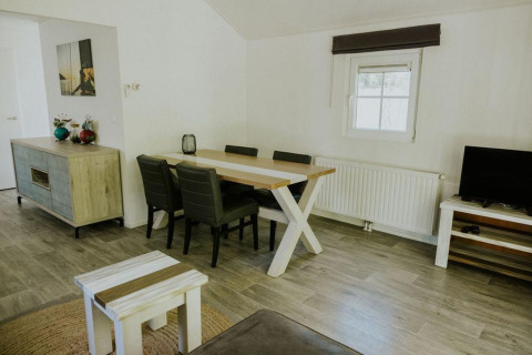 Sala moderna en Forest Lodge de Camping Si-Es-An, Países Bajos, con mesa de comedor, sillas y televisor.