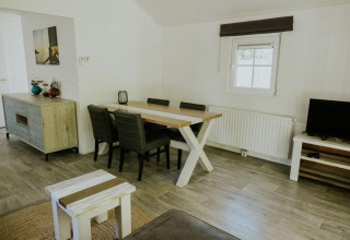 Sala moderna en Forest Lodge de Camping Si-Es-An, Países Bajos, con mesa de comedor, sillas y televisor.