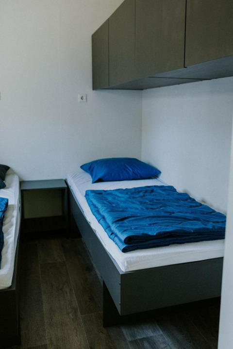 Habitación moderna con dos camas individuales, suelo de madera y ropa de cama azul en Forest Lodge, Camping Si-Es-An.