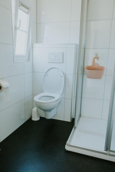 Et moderne badeværelse med et væghængt toilet, brusekabine og vindue på Camping Si-Es-An i Holland.