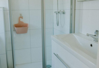 Salle de bain moderne avec douche vitrée, meuble lavabo blanc et miroir à Forest lodge, Camping Si-Es-An.