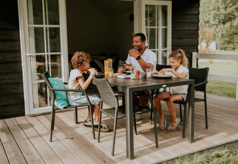En familie nyder et måltid sammen på terrassen foran Forest Lodge på Camping Si-Es-An i Holland.