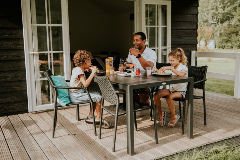 Eine Familie isst gemeinsam auf der Terrasse der Forest Lodge auf dem Campingplatz Si-Es-An in den Niederlanden.