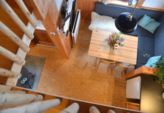 Vue du dessus d’une cabane confortable à Camping de Koeksebelt, avec table à manger, canapé et fleurs fraîches.