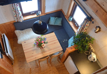 Knusse zithoek met hoekbank, eettafel, bloemen en ramen in een boomhut op Camping de Koeksebelt.