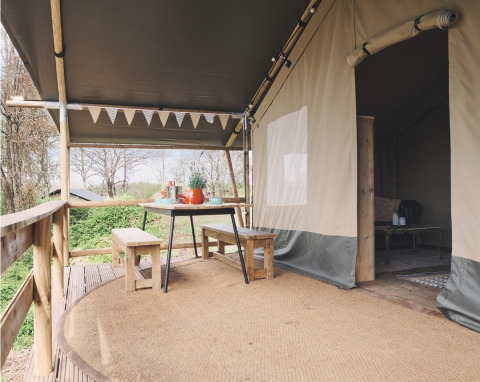 Safari-tent veranda met houten banken en tafel, buiten eten onder doek, zicht op de natuur.