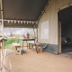 Safari tent deck with wooden benches and table, outdoor dining under canopy, surrounded by nature.