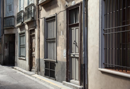 Calle estrecha cerca de Vindrac Alayrac, Occitania, Francia, con edificios antiguos y ventanas enrejadas.