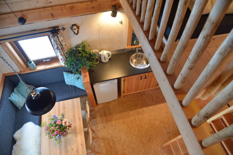 Top view of a cozy treehouse interior with dining area, kitchenette, and stairs at Camping de Koeksebelt.