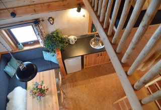 Vue d'en haut sur un intérieur de cabane dans les arbres avec coin repas, kitchenette et escalier en bois.