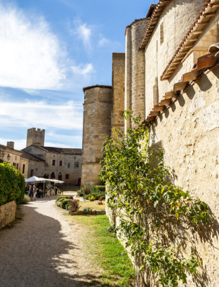 Sonniger Spazierweg mit Blick auf mittelalterliche Steinmauern und Gärten nahe Cazaubon in Occitanie, Frankreich.